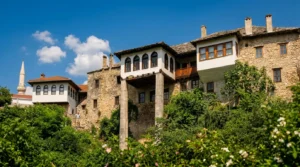 The traditional Bišćević House in Mostar with its distinctive wooden doksat (corner bay) rising on tall stone pillars above lush greenery