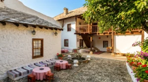 The inner courtyard (avlija) of the Bišćević House paved with river pebbles, with decorated tables, a wooden balcony, and the authentic atmosphere of old Mostar