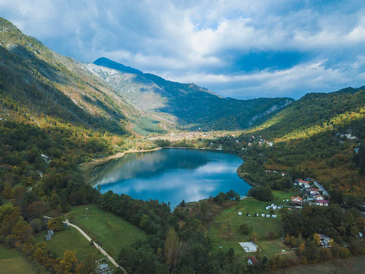 Aerial view of Boračko Lake in a mountain valley, green meadows and forests around the lake
