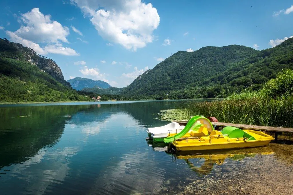 Colorful boats on the calm surface of Boračko Lake, mountains and greenery in the background