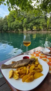 Čaša vina i riblje jelo servirana uz tirkiznu rijeku Unu na Japodskim otocima