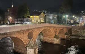Latinska ćuprija u Sarajevu noću, osvijetljeni kameni lukovi nad rijekom Miljackom