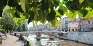 Latinska ćuprija u Sarajevu viđena kroz zeleno lišće, kameni lukovi iznad rijeke Miljacke