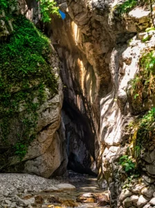 A narrow fissure and entrance to a dark cave and underground canyon between high, steep cliffs covered in green moss