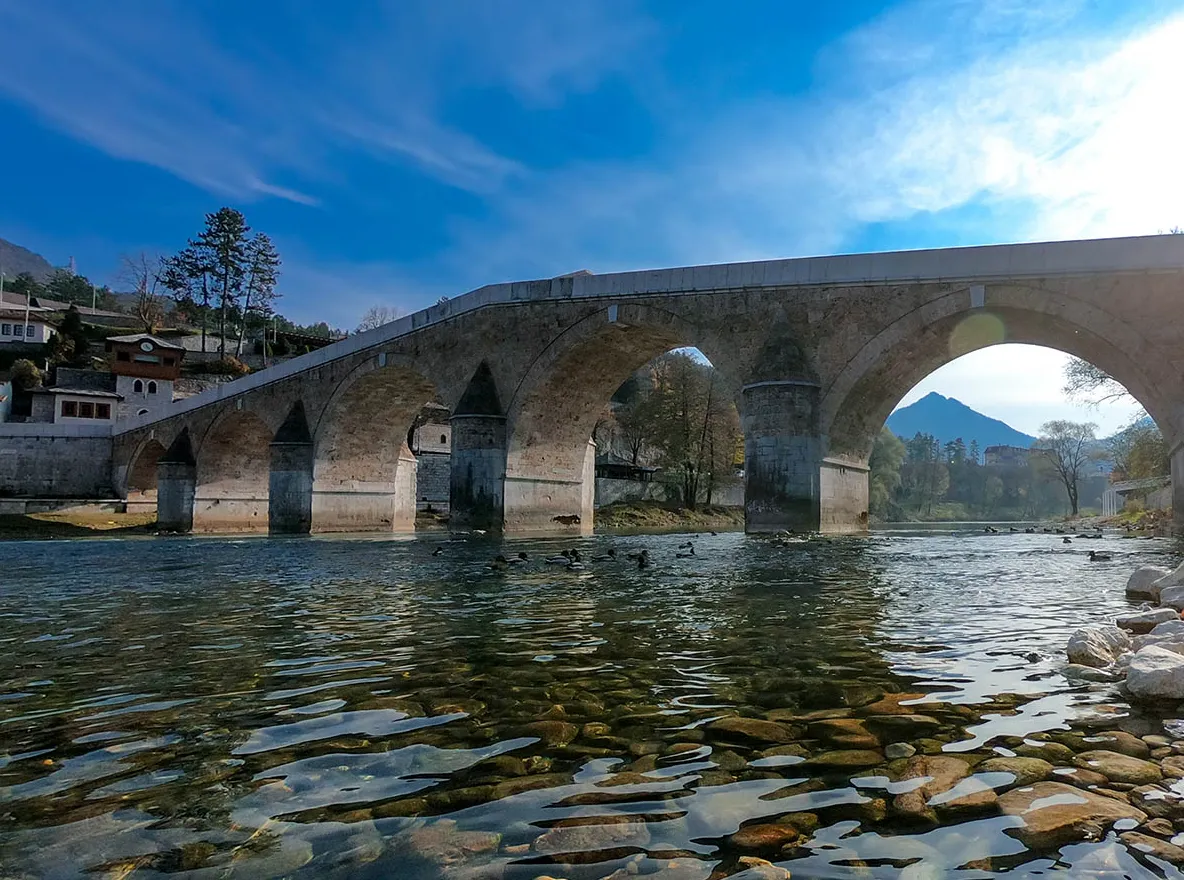 Frontalni pogled na Stari most u Konjicu, kameni lukovi iznad rijeke Neretve pod vedrim nebom