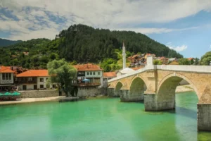 Bočni pogled na Stari most u Konjicu, kameni lukovi nad tirkiznom Neretvom okruženi zelenilom