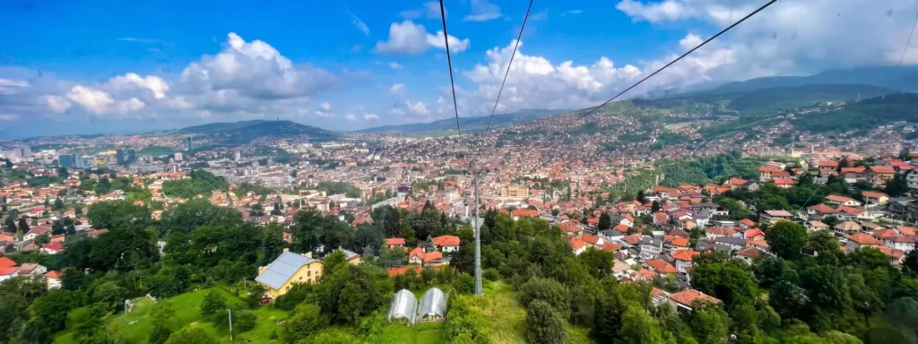 Panoramski pogled na Sarajevo sa Vidikovca Trebević, gondola žičare u prvom planu i grad u dolini okružen planinama