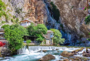 View of the Blagaj Tekke and the Buna River Spring, with historic stone buildings nestled beneath a towering rocky cliff