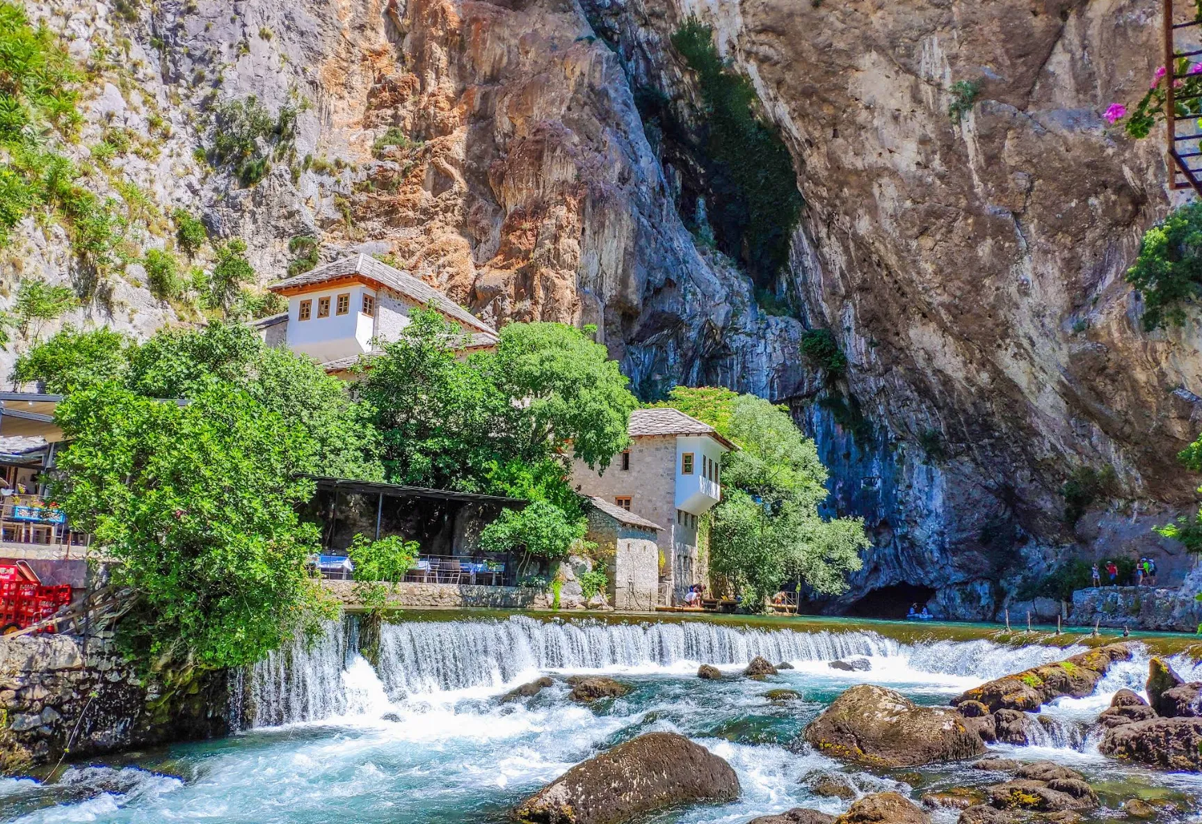 View of the Blagaj Tekke and the Buna River Spring, with historic stone buildings nestled beneath a towering rocky cliff
