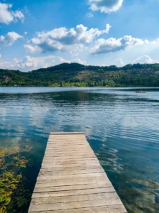 A wooden pier leading into the water of Kop Plane-Šići Lake with hills in the background