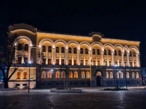 Veličanstvena prednja fasada Banskog dvora u Banjoj Luci, obasjana dekorativnom toplom žutom rasvjetom tokom noći na praznom gradskom trgu