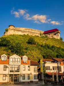 Doboj kalesinin şehir yapılarının üzerinde, tepe zirvesinde yükselen masif taş surları; bulutlarla bezeli açık bir gökyüzü altında