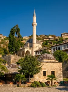 A view of the stone structure of Hadži-Alijina džamija with its distinctive domes and slender minaret, surrounded by traditional stone houses on the hill
