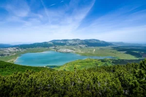 Panoramski pogled na Jezero Blidinje okruženo zelenim planinama pod vedrim plavim nebom