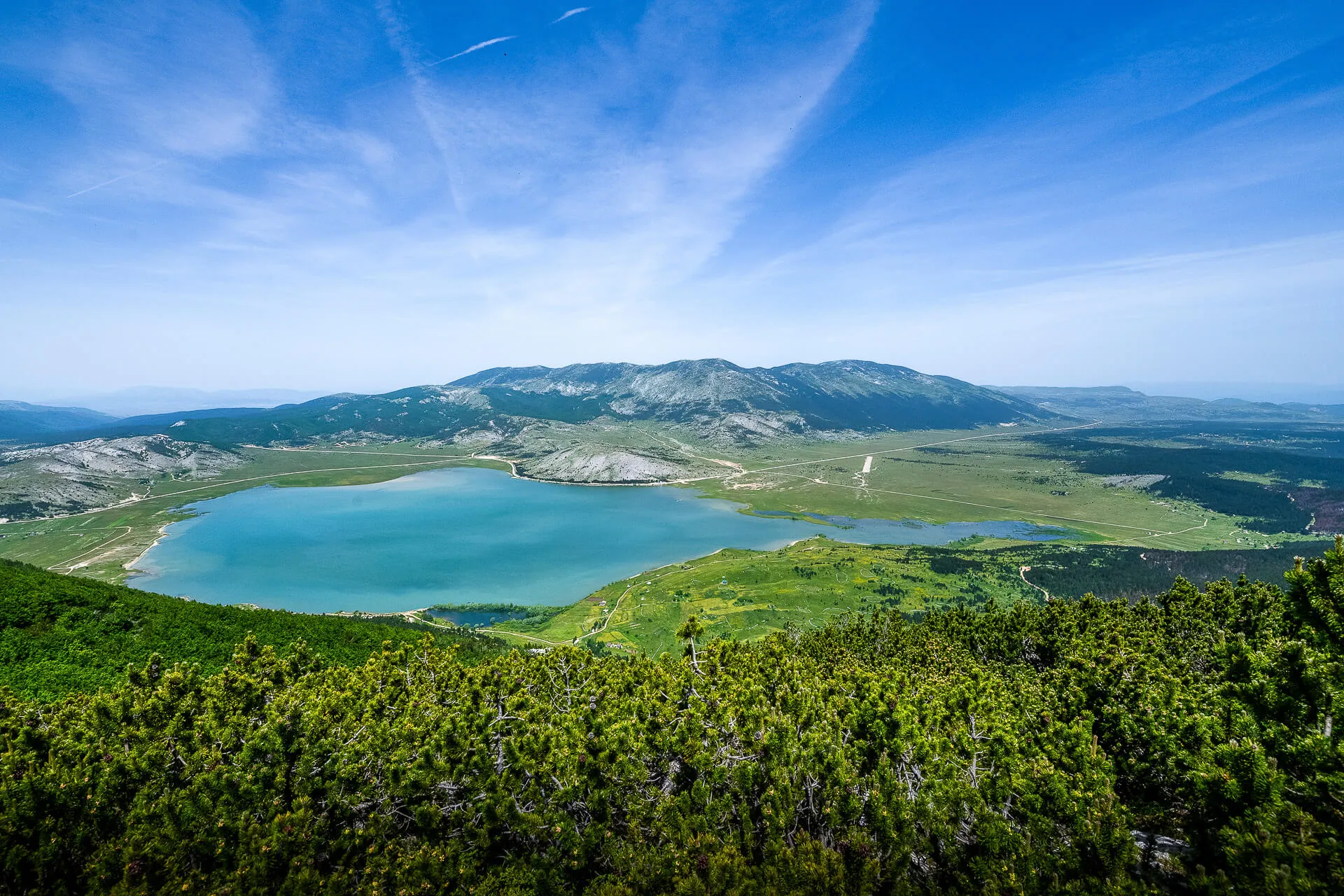 Panoramski pogled na Jezero Blidinje okruženo zelenim planinama pod vedrim plavim nebom