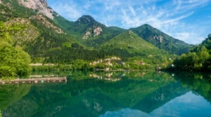 Mirna, staklata površina vještačkog jezera Grabovica u kojoj se savršeno ogledaju visoke, šumovite zelene planine i vedro nebo sa par bijelih oblaka