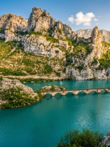 Panoramski pogled sa visine na smaragdno-plavo jezero Grabovica preko kojeg se proteže stari kameni vijadukt sa lukovima, podno strmih i masivnih sivih litica kanzona Neretve