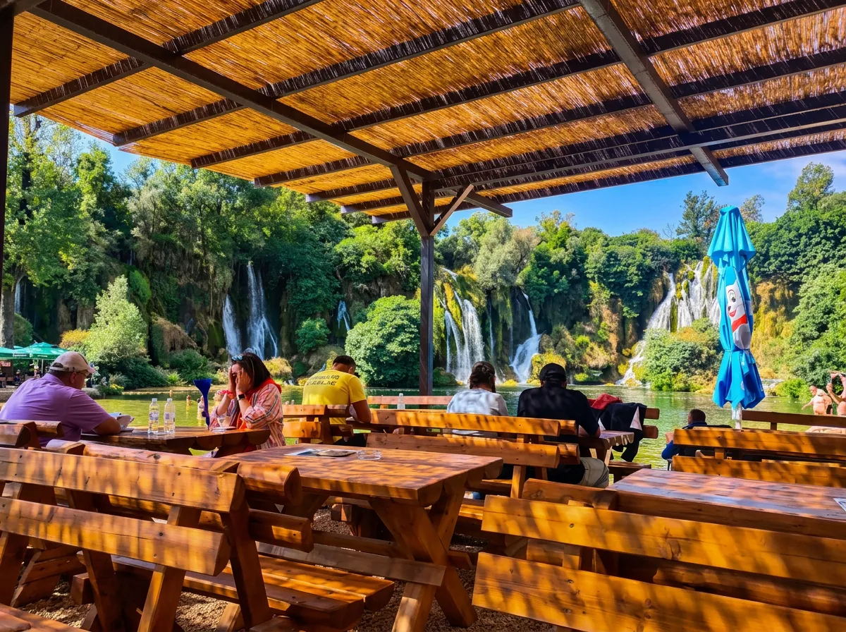 Blick von der sonnigen Holzterrasse des Restaurants unter einem Strohdach auf die Gäste, die an den Tischen sitzen und den Blick auf die Wasserfälle im Hintergrund genießen