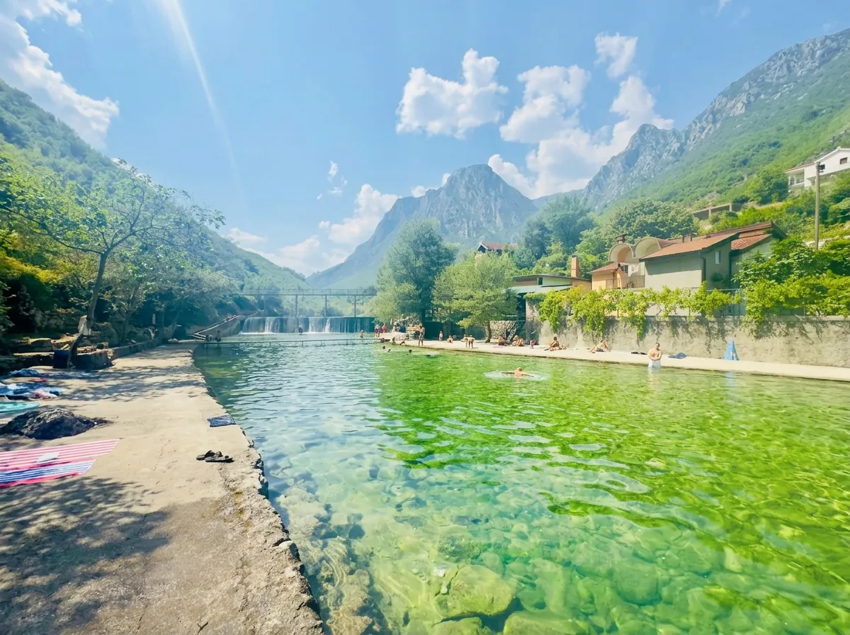 Geräumiger und gepflegter Badeplatz mit kristallklarem und flachem grünem Wasser, betoniertem Zugang für Badegäste und Blick auf eine Bergschlucht in der Ferne unter sonnigem Himmel
