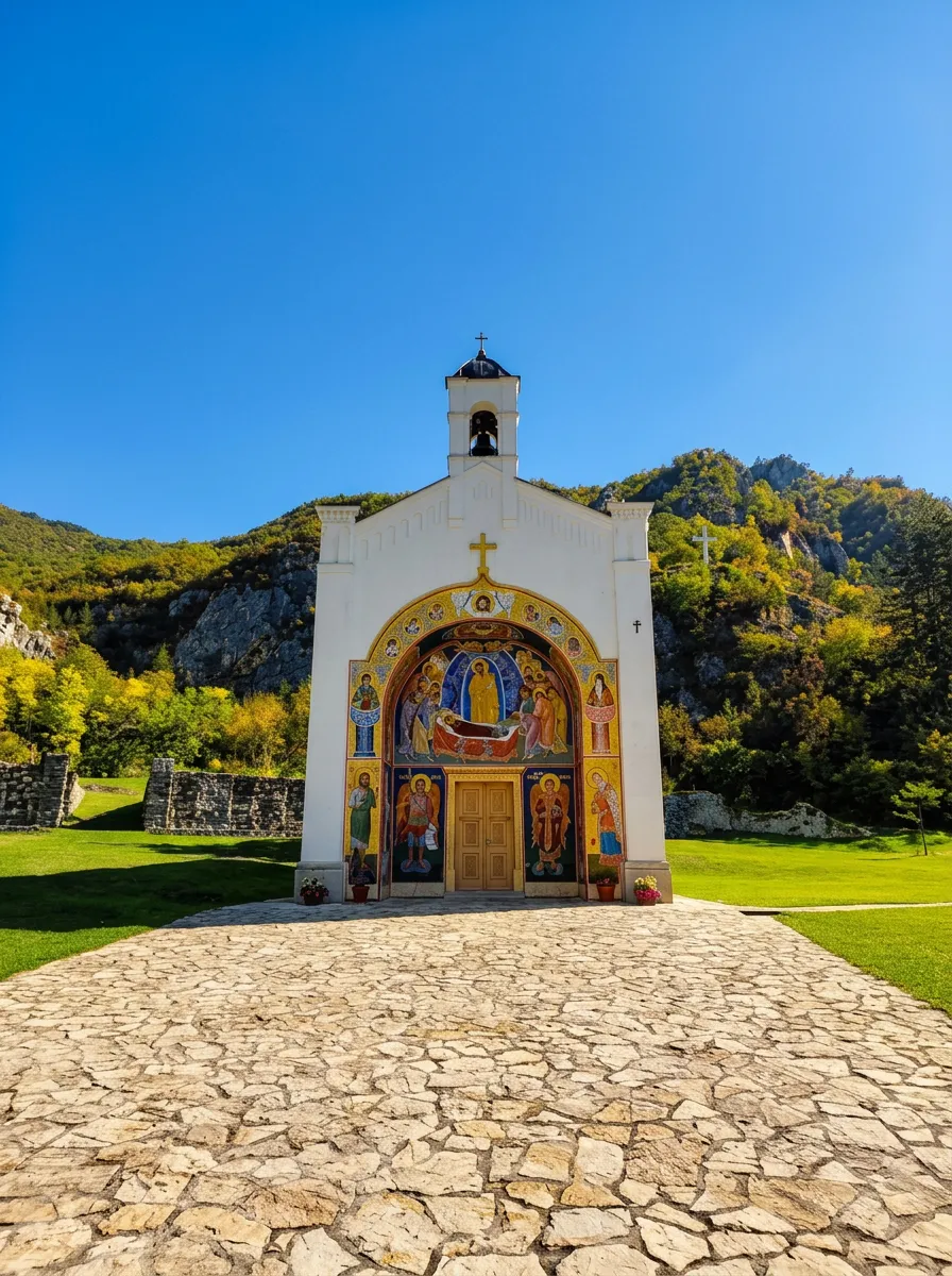 A stone path leading to the white facade of the monastery church in Dobrun, with a large, vivid fresco above the entrance door under the open sky