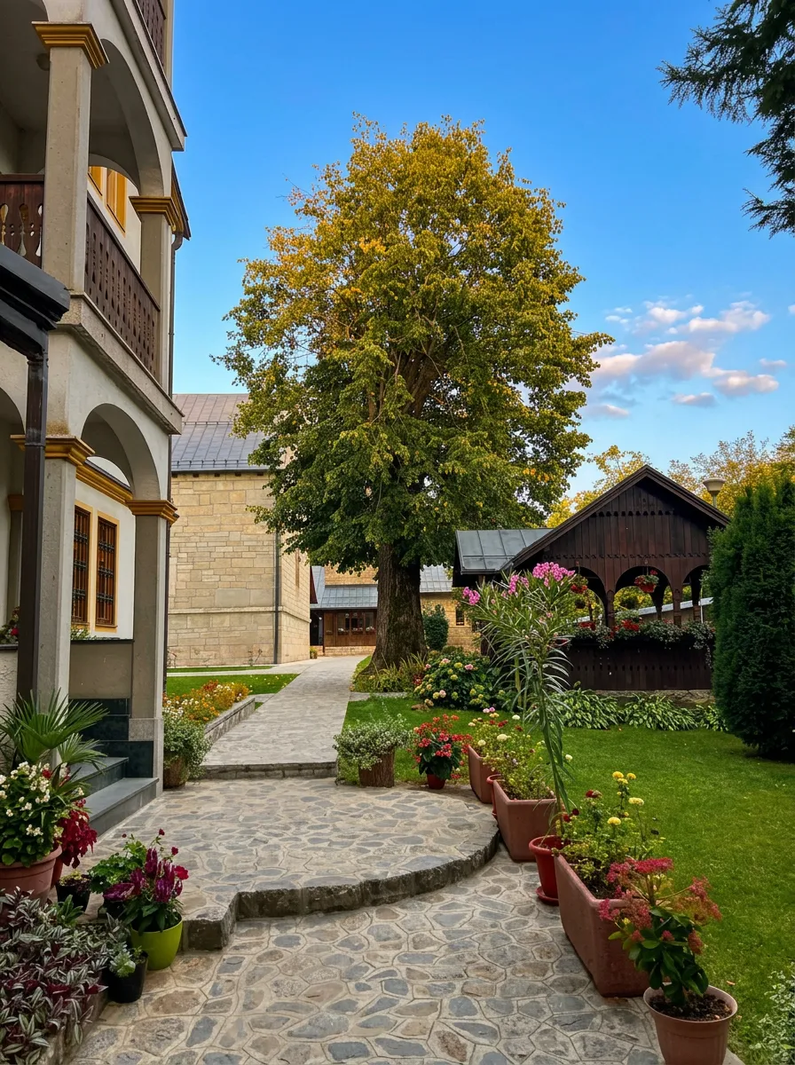 sentiero lastricato in pietra che attraversa il curato cortile del monastero con prato verde, vasi di fiori, un portico in legno e un grande albero davanti all’edificio in pietra