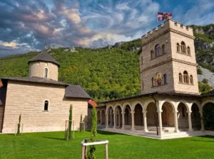 A close-up of the monastery church and residence with open semicircular arches (a porch) and a massive stone tower, under a dynamic blue sky with white clouds