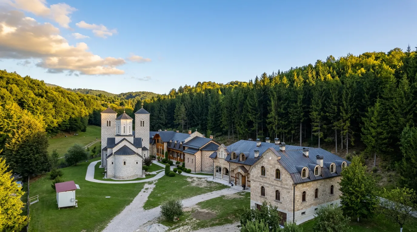 Pogled iz ptičije perspektive na cijeli kompleks manastira Stuplje, koji obuhvata bijelu crkvu sa zvonikom, pješačke staze i dugačke kamene konake smještene u prelijepoj dolini okruženoj gustom šumom