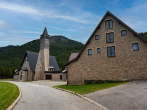 Die asphaltierte Zufahrtsstraße, die zur modernen Steinkirche des Heiligen Elias und dem dazugehörigen Gebäude mit klaren Linien führt, eingebettet in die Berglandschaft von Blidinje