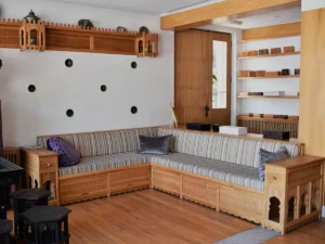 A view of the interior with comfortable corner sećijas made of light wood with a striped pattern, matched with a wooden floor and shelves in an authentic Bosnian style