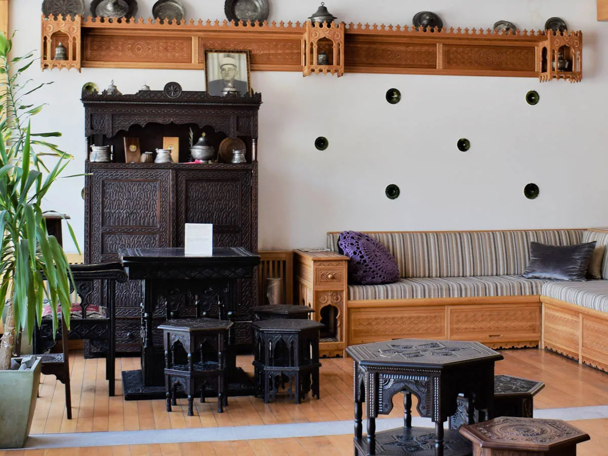 An exhibition space with unique pieces of hand-carved furniture, including dark wooden cabinets, small tables (peškune), and a traditional sećija with decorative cushions