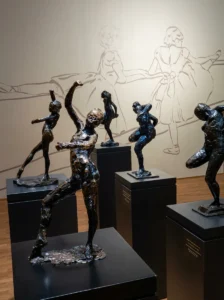 An arrangement of bronze and dark sculptures depicting human figures in motion, displayed on black pedestals inside the gallery of the Museum of Contemporary Art