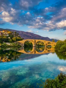 Panoramski pogled na Arslanagića most v sončnem dnevu, obdan z zelenjem in hribi