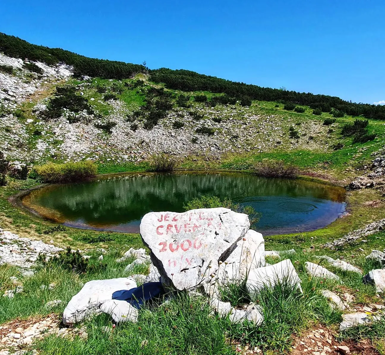 Malo planinsko jezerce na Čvrsnici okruženo kamenjem i travom, bijeli kamen u prvom planu