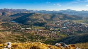Široka panorama grada Trebinja i vijugavog toka rijeke Trebišnjice u ravnici, uslikana sa krševitog vrha planine Leotar pod plavim nebom