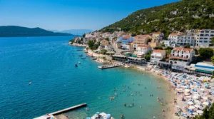A beautiful panoramic bird's-eye view of the Neum coastline, turquoise-blue sea with swimmers, small piers, and densely built hotels and apartments along the hillside