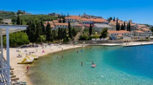 A high-angle view of Zenit Beach in Neum with clean, clear turquoise water enjoyed by swimmers, while coastal buildings and Mediterranean vegetation can be seen in the background