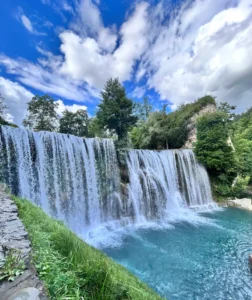 Frontalni pogled na Plivski vodopad u Jajcu, široki slapovi bijele pjene pod vedrim nebom
