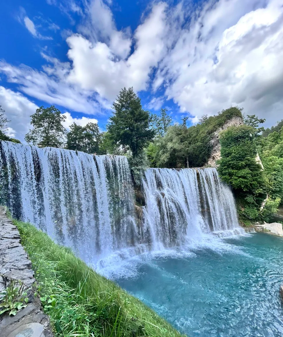 Frontalni pogled na Plivski vodopad u Jajcu, široki slapovi bijele pjene pod vedrim nebom