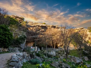 Natural entrance to Ravlića Cave surrounded by rocks and vegetation