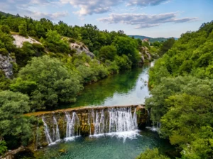 View from an elevated point of the wide waterfall of the Sušica River, where the water plunges in several smaller streams over a travertine barrier into a deep green mountain pool