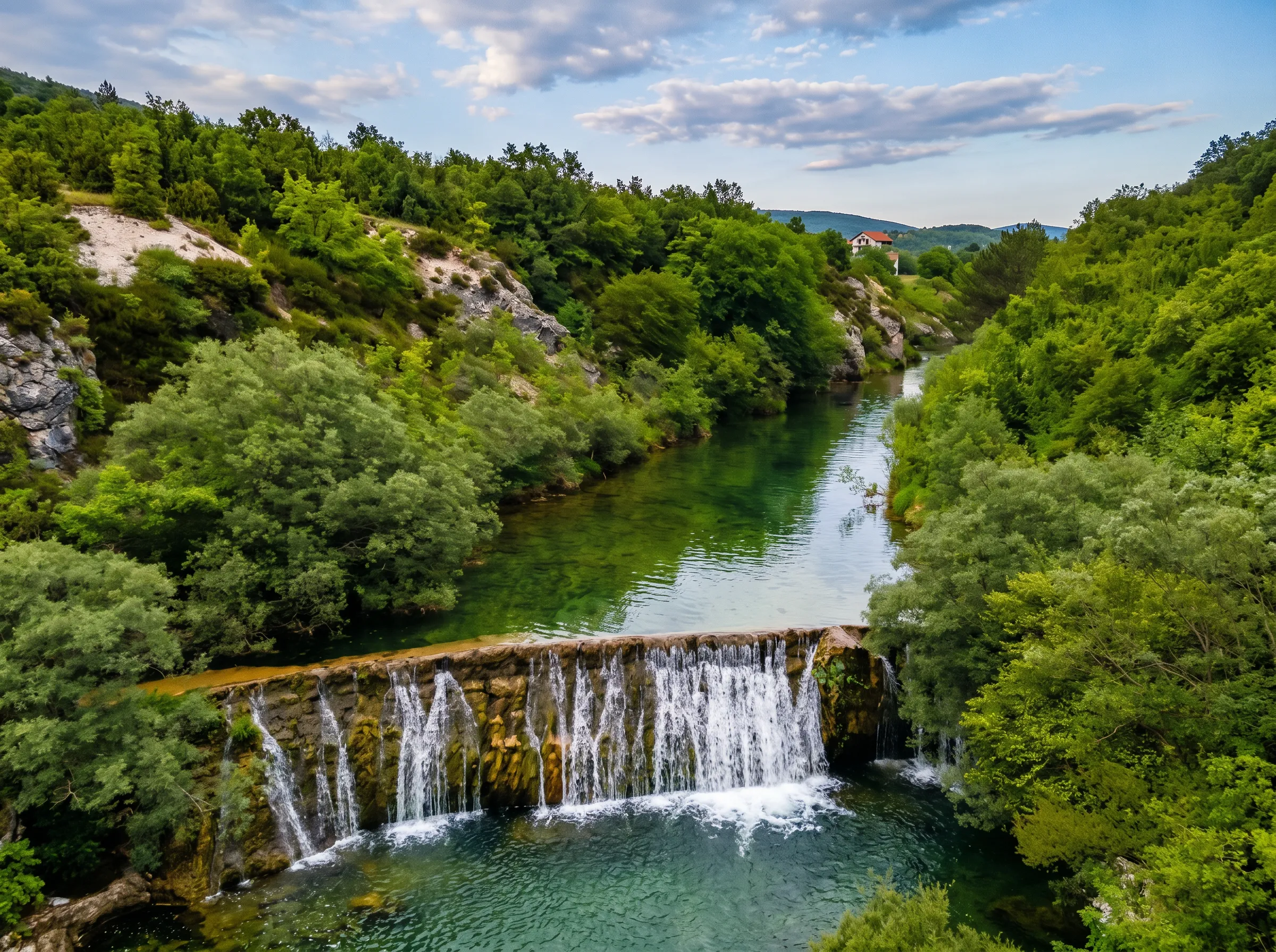View from an elevated point of the wide waterfall of the Sušica River, where the water plunges in several smaller streams over a travertine barrier into a deep green mountain pool