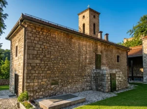 Bočna strana Stare pravoslavne crkve građena od klesanog kamena sa zvonikom u pozadini, okružena uređenim dvorištem sa sitnim šljunkom
