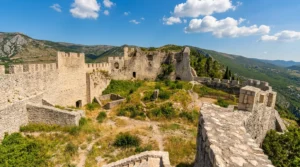 Pogled na prostrano notranje dvorišče in ostanke kamnitih obzidij Stjepan-grada v Blagaju pod modrim nebom z belimi oblaki