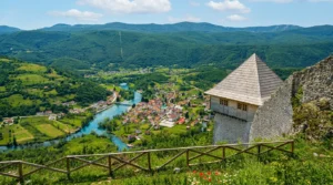 A panoramic view from the lookout point of Ostrovica fortress over the picturesque settlement of Kulen Vakuf in the valley and the emerald-green flow of the Una River, with a wooden safety railing in the foreground