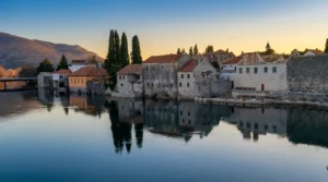 Traditional stone houses and the walls of the Old Town in Trebinje perfectly reflected in the calm surface of the Trebišnjica River during a gentle sunset