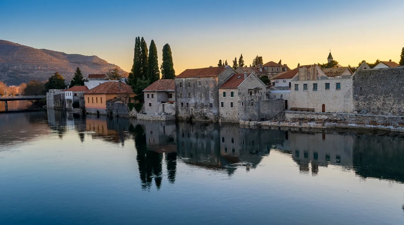 Traditional stone houses and the walls of the Old Town in Trebinje perfectly reflected in the calm surface of the Trebišnjica River during a gentle sunset