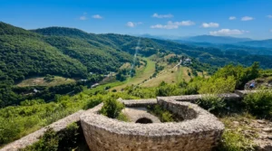 Pogled sa polukružnog kamenog bedema tvrđave prema prostranoj zelenoj dolini, okolnim brdima i seoskim predjelima koji se protežu u daljini pod sunčanim nebom