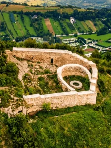 Snimak iz ptičije perspektive koji prikazuje tlocrt i rekonstruisane kamene zidine istorijskog kraljevskog grada Visoki, smještenog na samom vrhu zelenog i šumovitog brda