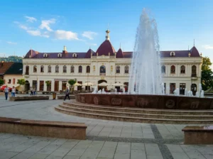 View from the paved promenade of the central circular fountain and the monumental yellow Barok building with its distinctive red roof and domes on Trg slobode in Tuzla