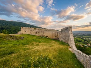 Preserved stone defensive walls of Sokolac Fortress surrounding the inner grassy courtyard, under a sky streaked with warm evening clouds at dusk